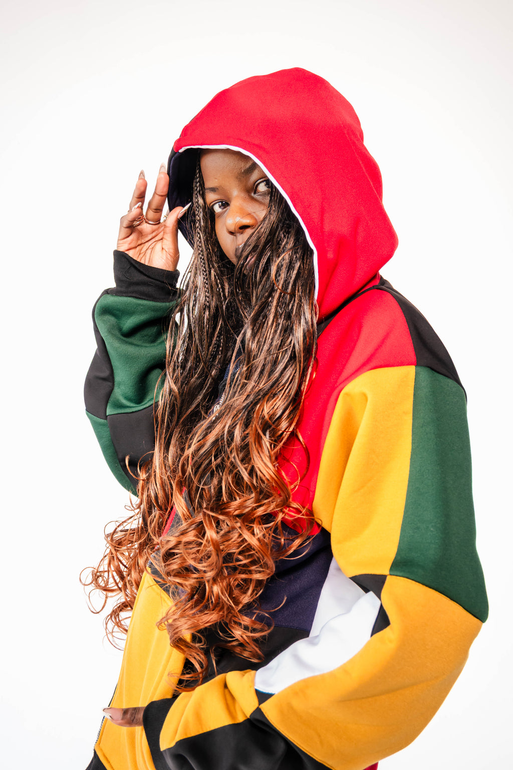 A model wearing a colorful patchwork hoodie made in red, green, yellow, blue, black, and white panels, with a two coloured hood.